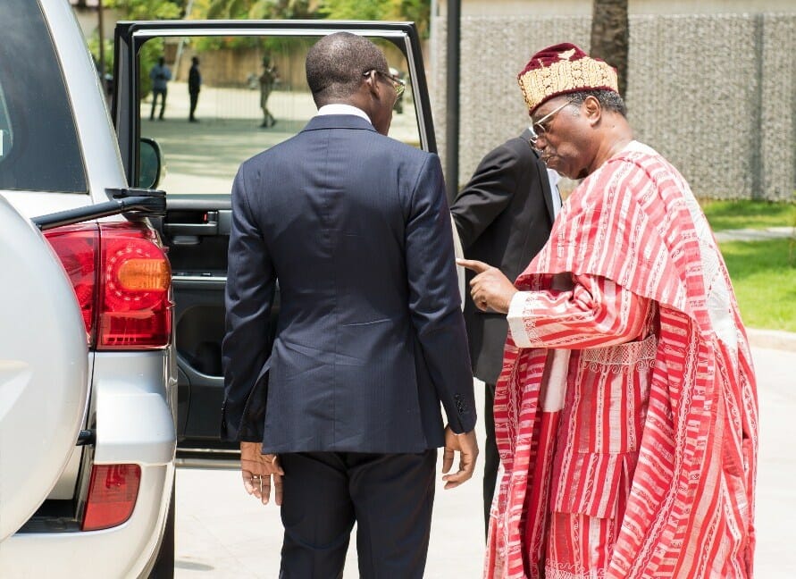 After breaching protocol by shaking President Talon's hand while seated, an embarrassed former president Soglo, right, follows Talon to his residence, allegedly to plead his son's case.