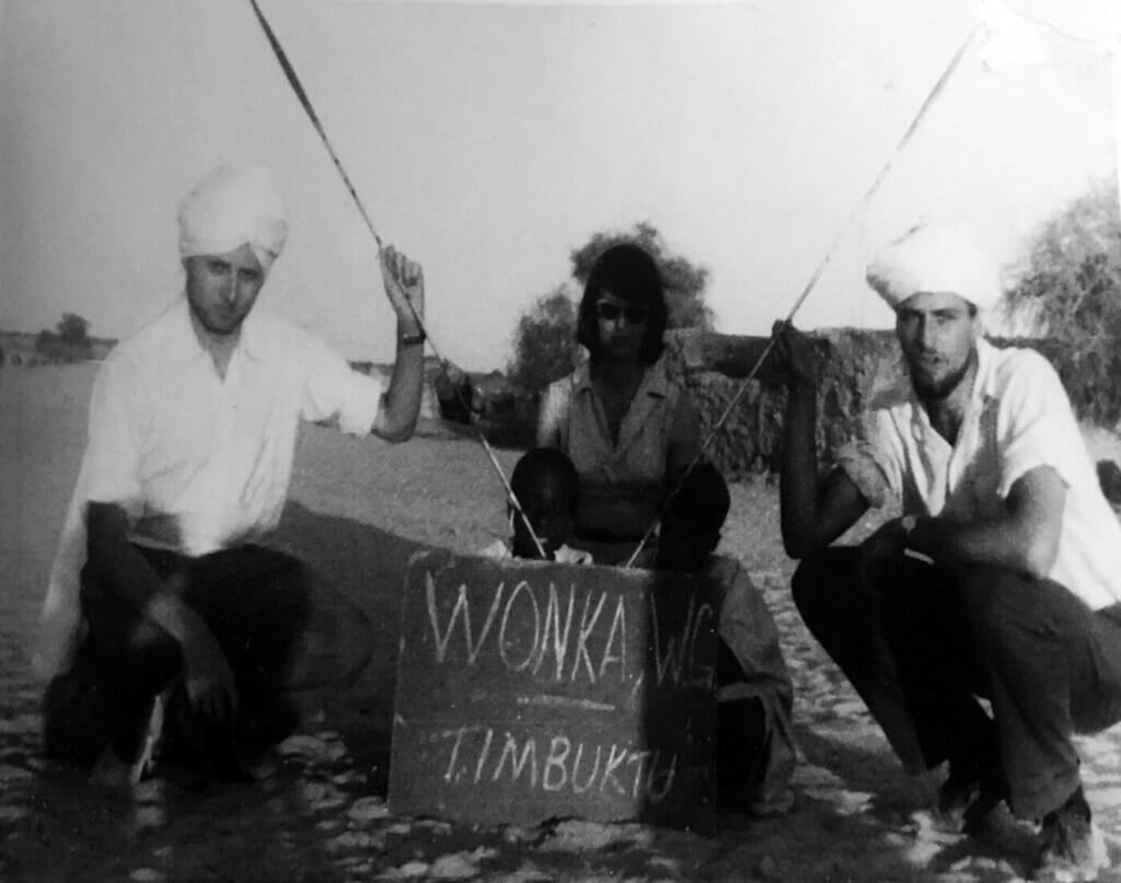 This picture was shot in 1960 during the visit of Jeffrey Fadiman, then a 24-year-old student at Stanford University, in Timbuktu. Left to right: George Chester, Andee Whitney, and Jeff Fadiman. The sign: Warren G. Wonka is a mythical Stanford Student, who magically appears everywhere on earth. The blackboard is a nod to that tradition.