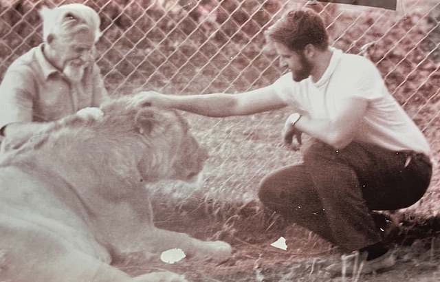 Audaciously petting a lion in the company of his buddy John